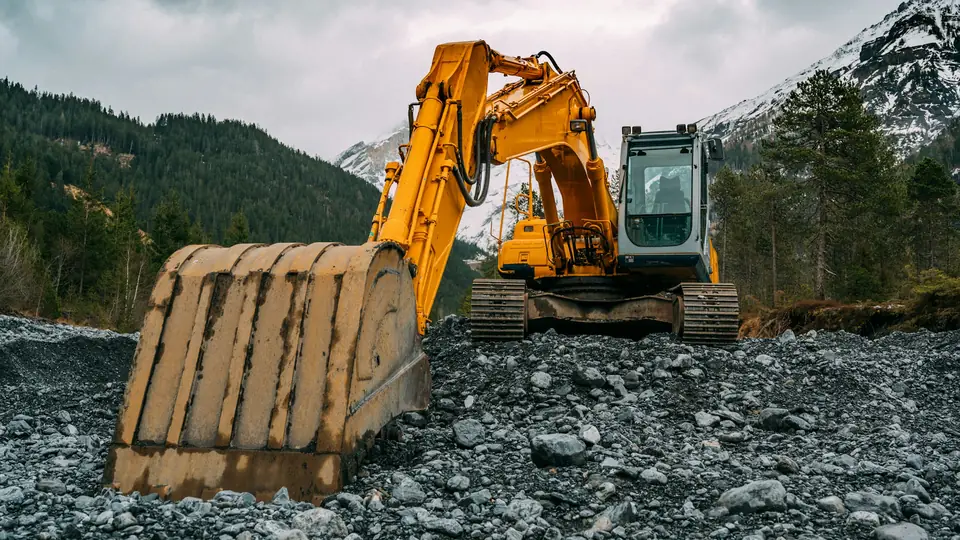 Gul bandgrävare med stor skopa på en grusplan vid skogen