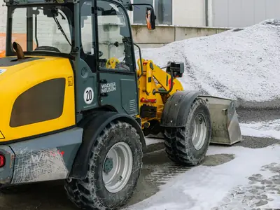 Kompakt hjullastare med skopa vid en snöhög