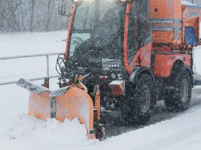 Orange redskapsbärare plogar en snöig gångväg