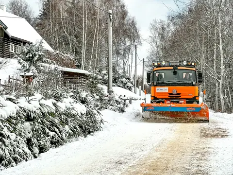 Orange plogbil röjer en snötäckt väg genom skogen